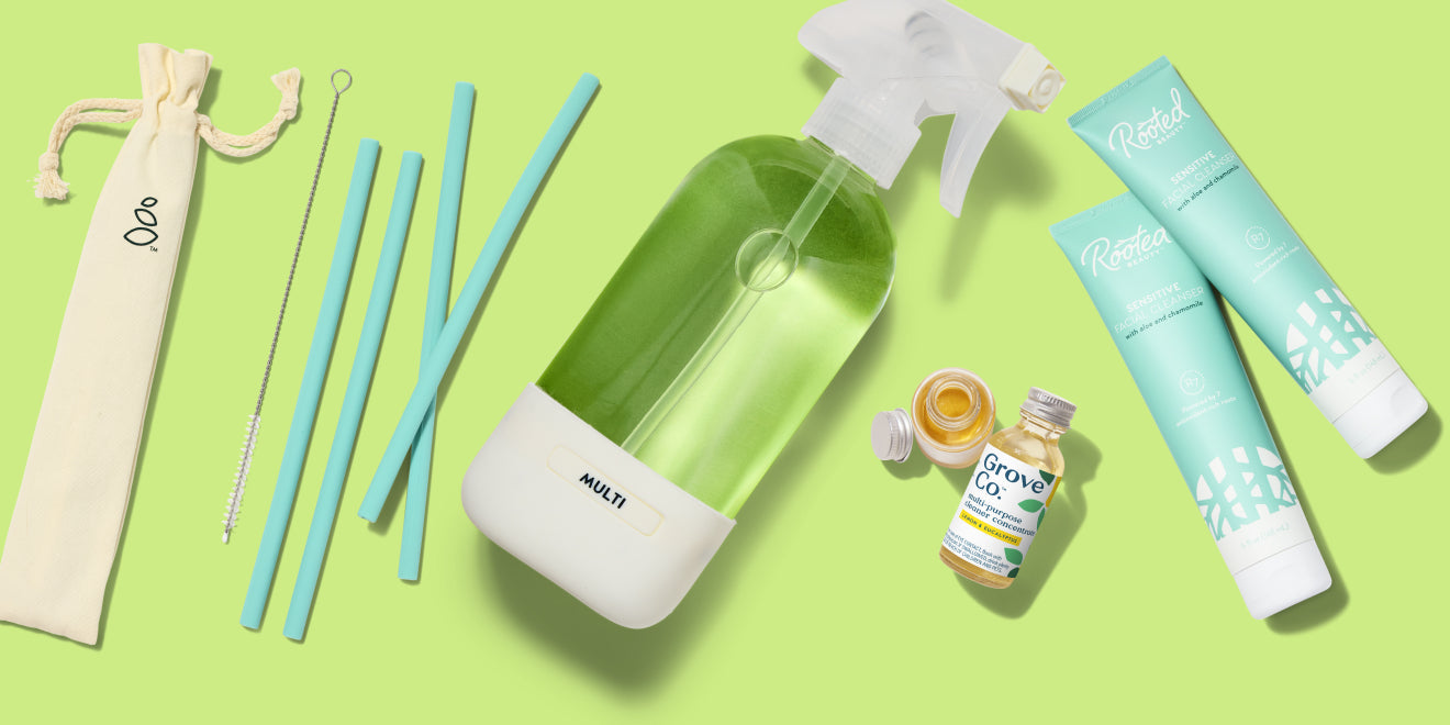 A reusable straw set, a spray bottle with green liquid, a small glass bottle, and two blue-green tubes are arranged on a light green background.