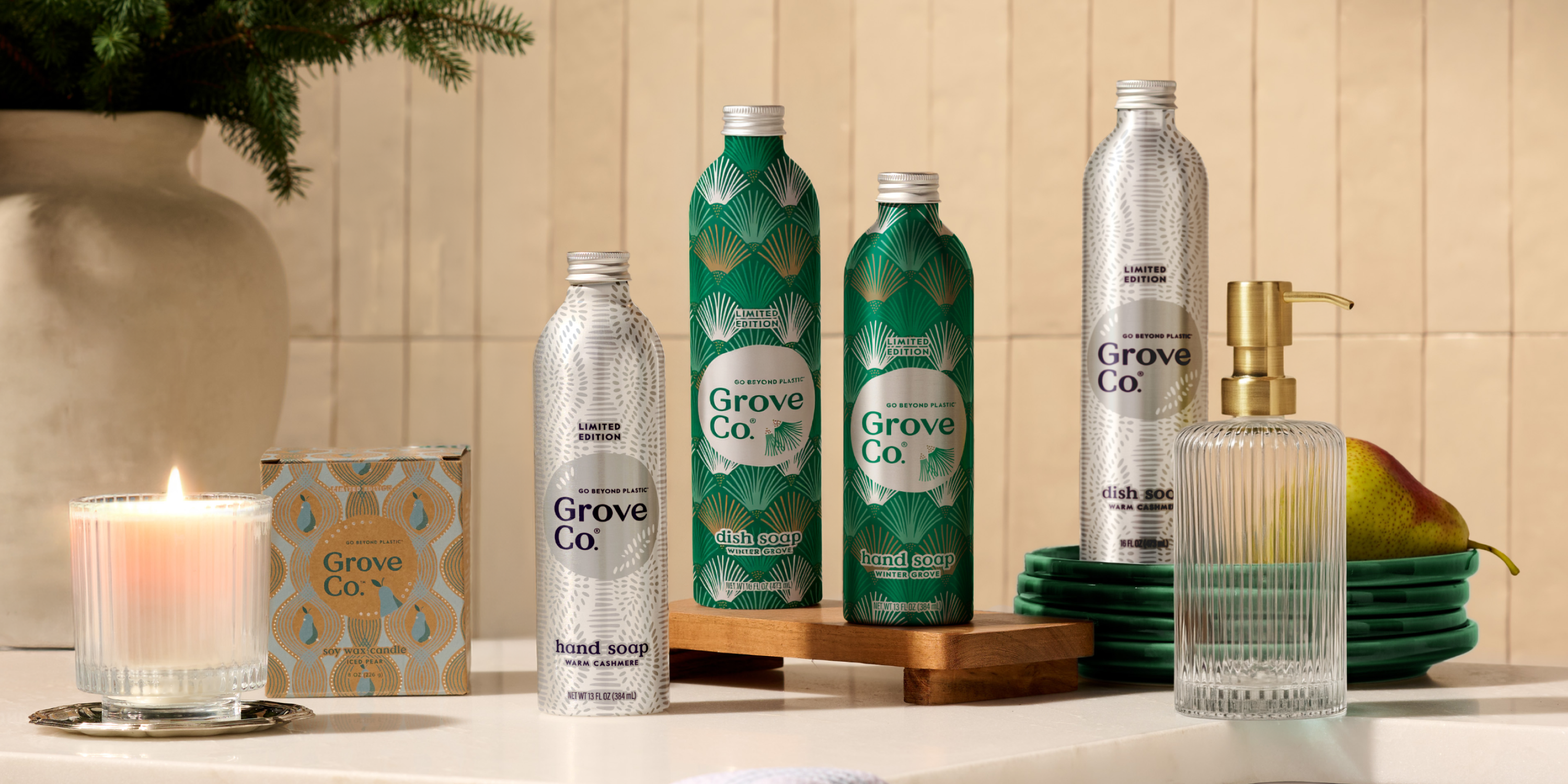 Grove Co. dish soap and hand soap bottles on a kitchen counter with a candle lit.