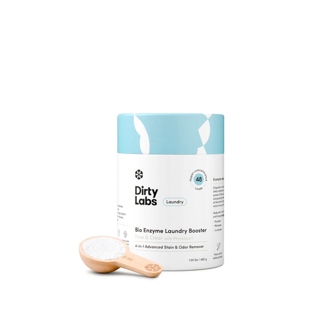 A container of Dirty Labs Bio Enzyme Laundry Booster is displayed on a white background, featuring advanced enzyme technology, with a wooden scoop filled with white powder positioned in front of the container.