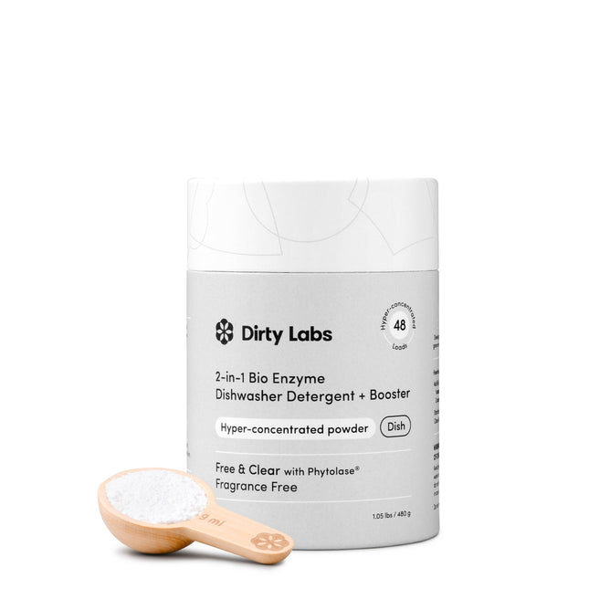A container of Dirty Labs 2-in-1 Bio Enzyme Dishwasher Detergent + Booster is displayed beside a wooden scoop filled with the white powdered detergent, highlighting the effective 2-in-1 powder formula against a clean white background.