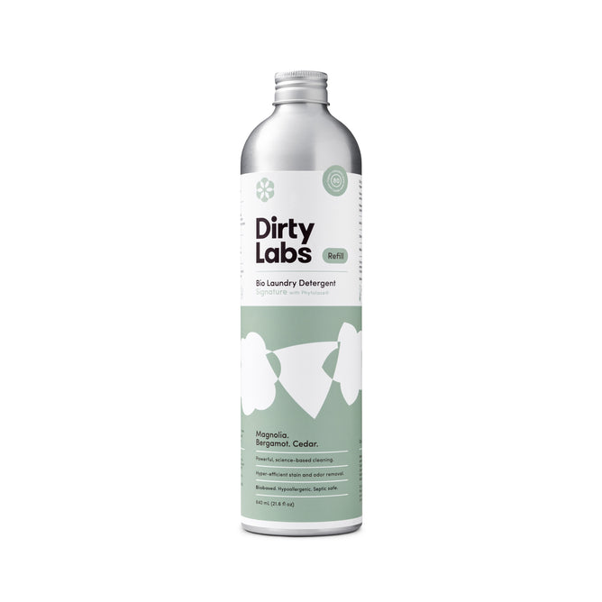 A silver bottle of Dirty Labs Bio Laundry Detergent with Phytolase®—Magnolia, Bergamot, Cedar—featuring a green label with white text and floral graphics. This natural detergent is scented with magnolia, bergamot, and cedar.
