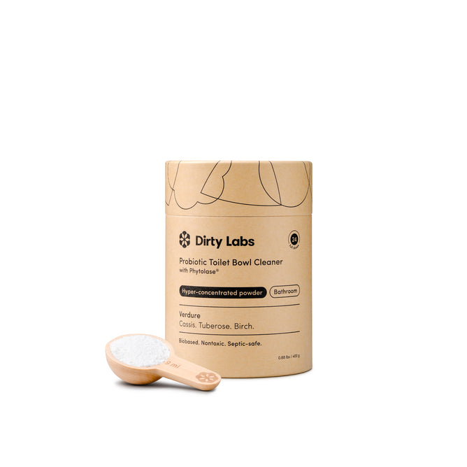 Dirty Labs Probiotic Toilet Bowl Cleaner with Phytolase® comes in a cylindrical cardboard container with a wooden scoop and white powder. Its minimalist, eco-friendly packaging emphasizes deep cleaning power using Phytolase® bioenzyme technology.