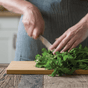 Wearing a striped apron, a person chops fresh cilantro on the Bambu Undercut Bamboo Cutting Board in a kitchen setting.