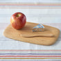 A red apple, foil-wrapped cheese wedge, and wooden spreader rest on the Bambu Classic Bamboo Cutting Board atop a striped tablecloth.