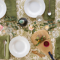 A table set with white bowls, green napkins, silver cutlery, wine glasses, flowers, candles, and the Bambu Artisan Droplet Cutting & Serving Board holding figs, a lemon, and a small red dish.