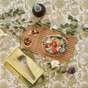 A flatbread with spinach, ricotta, and tomatoes is presented on the Bambu Essential Bread Cutting Board, surrounded by figs, nuts, wine, glassware, green napkins with forks, flowers, and greenery atop a patterned tablecloth.