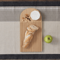 The Bambu Essential Bread Cutting Board holds a sliced baguette, mixed nuts, and a round of soft cheese. Next to the eco-friendly board, an apple rests on a beige and gray woven placemat.