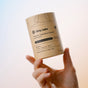 A hand holds a cylindrical Dirty Labs Probiotic Toilet Bowl Cleaner with Phytolase®, featuring brown minimalist packaging against a light background. The label highlights its bioenzyme technology for deep toilet bowl cleaning.