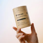 A hand holds a cylindrical container labeled “Dirty Labs Probiotic Toilet Bowl Cleaner with Phytolase®,” featuring ingredients and product information on a tan background, and showcasing its advanced Phytolase® bioenzyme technology for deep cleaning toilet bowl care.