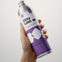 A hand holds a silver and purple bottle of Dirty Labs Bio Laundry Detergent with Phytolase® in Jasmine, Matcha, and Vetiver scent, labeled as a refill. The natural laundry detergent features simple geometric shapes and text on its label.