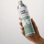 A hand holds a silver bottle labeled "Dirty Labs Bio Laundry Detergent with Phytolase® - Magnolia, Bergamot, Cedar," featuring green and white graphics. The minimalist design and eco-friendly branding make this natural detergent from Dirty Labs an excellent choice for those seeking environmentally conscious laundry supplies.