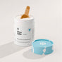An open Dirty Labs Bio Enzyme Laundry Booster container, featuring a white design and a blue lid set aside, reveals powder inside with a wooden scoop. Developed with advanced enzyme technology to target biological stains, the product rests on a light surface.
