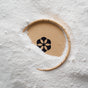 A wooden circular frame dusted with white powder reveals a black flower design on a tan surface—much like the deep cleaning effect of Dirty Labs Probiotic Toilet Bowl Cleaner with Phytolase®.