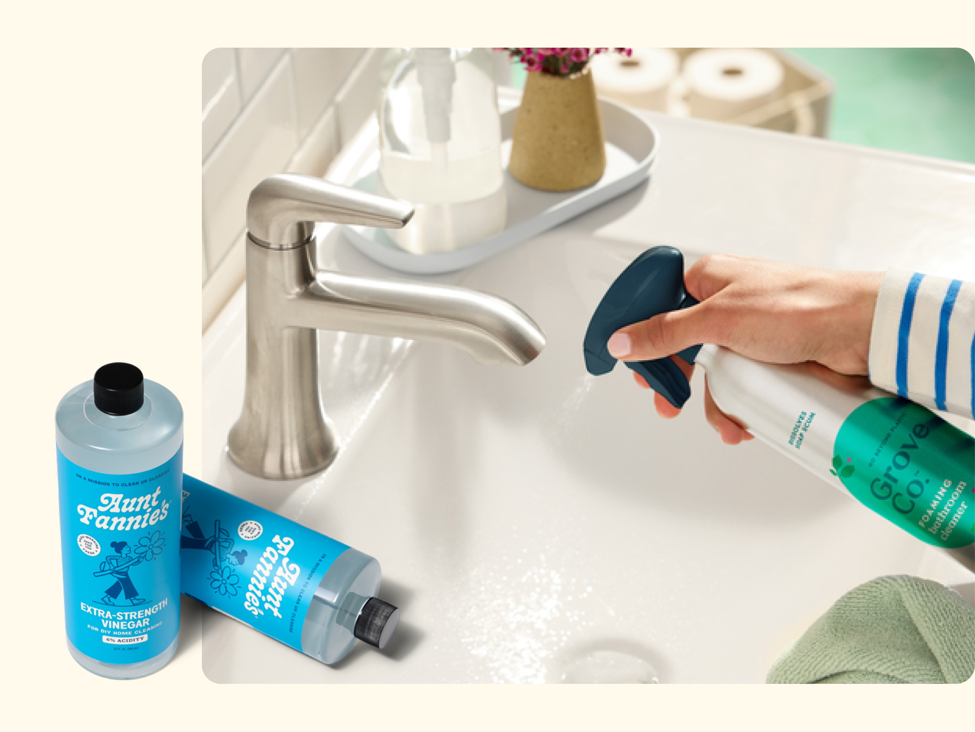 A hand sprays cleaner onto a bathroom sink with a silver faucet. On the counter are soap and decor. In the foreground are bottles of Aunt Fannies vinegar and Grove Co. cleaner.