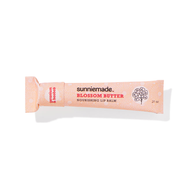 A pink paper squeeze tube labeled Sunniemade Nourishing Lip Balm - Blossom Butter, featuring a floral design and white polka dots, is shown on a white background.