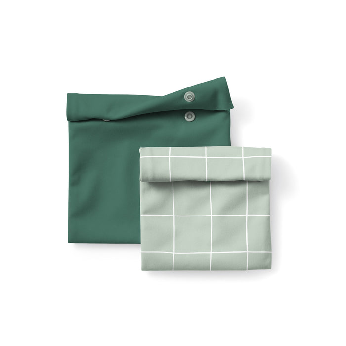 The Esembly Baby Reusable Snack & Sammy Food Pouches, 2-pack, feature two standing bags—one solid dark green with snap buttons and one light green with a white grid—offering a stylish landfill-free alternative for your waste-free lunchbox.