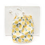 A white drawstring bag with yellow lemons and green leaves rests on a white placemat beside a small round object—ideal for storing your Esembly Baby Reusable Paper Towel Set (100% organic, unbleached).