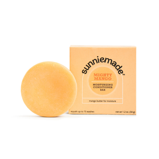 A round, orange Sunniemade Moisturizing Conditioner Bar - Mighty Mango rests next to its matching box. The simple, plastic-free packaging highlights the nourishing mango butter inside for added moisture.