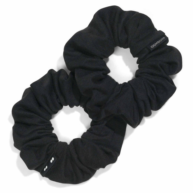 Two black KOOSHOO Scrunchies made from organic cotton rest on a white background, slightly overlapping. One features a small tag with text.