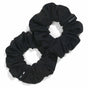 Two black KOOSHOO Scrunchies made from organic cotton rest on a white background, slightly overlapping. One features a small tag with text.