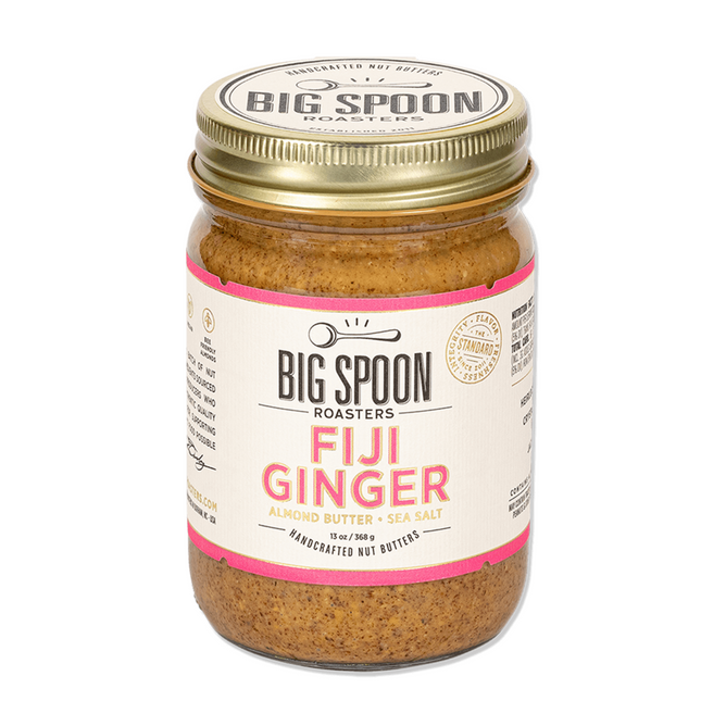 A glass jar of Big Spoon Roasters Fiji Ginger Almond Butter, made with sustainable ginger and sea salt, featuring a gold lid and a cream label with black and pink text.