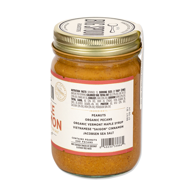 A glass jar of Big Spoon Roasters Maple Cinnamon Peanut & Pecan Butter features a gold lid and a label noting organic pecans, Vermont maple syrup, Vietnamese cinnamon, and Jacobsen sea salt.