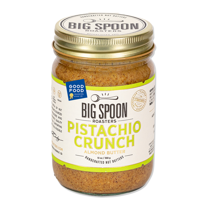 A jar of Big Spoon Roasters Pistachio Crunch Almond Butter features a gold lid, white label with green and yellow text, Good Food Awards sticker, and highlights premium flavor from heirloom Mission almonds and California pistachios.