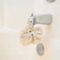A Me Mother Earth Reusable Sisal Shower Pouf in a natural color hangs by a ribbon from a silver bathtub faucet in a white tub.