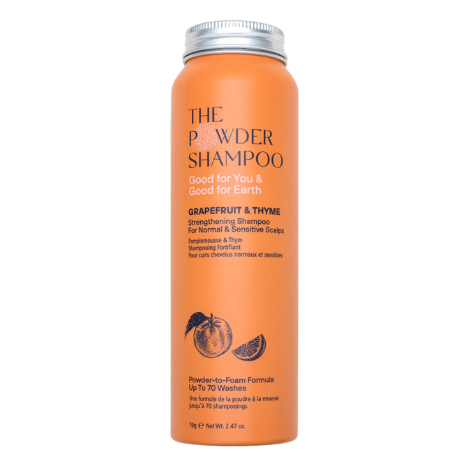An orange cylindrical bottle labeled The Powder Shampoo Strengthening & Soothing Powder Shampoo for normal and sensitive scalps features fruit illustrations and text about its powder-to-foam formula that supports scalp balance.