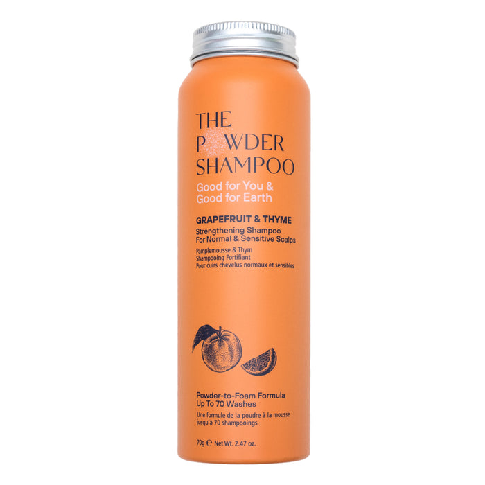 An orange cylindrical bottle labeled The Powder Shampoo Strengthening & Soothing Powder Shampoo for normal and sensitive scalps features fruit illustrations and text about its powder-to-foam formula that supports scalp balance.