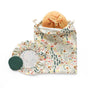 A round sourdough loaf peeks from a nature-themed drawstring bag, part of the Sourdough Proofing Kit by Esembly Baby. Next to it are two fabric covers from the kit, one with a clear window and one solid green, all on a white background.