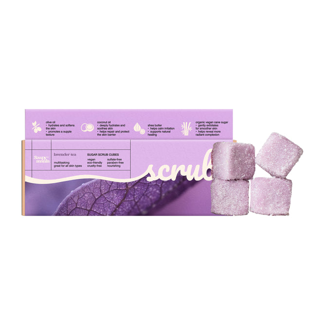A box of Soapymania Lavender Tea Sugar Scrub Cubes sits beside four purple cubes. The vegan packaging highlights key ingredients and benefits, and features a leaf image.