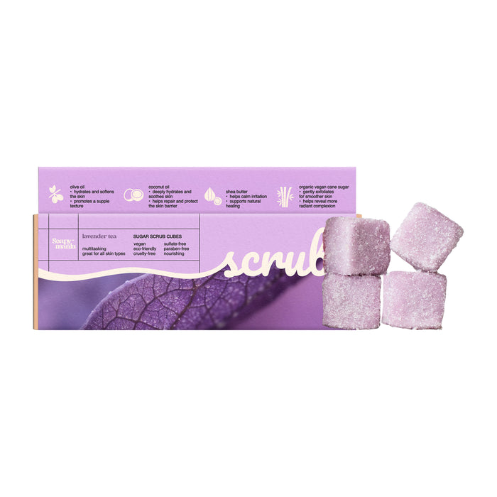 A box of Soapymania Lavender Tea Sugar Scrub Cubes sits beside four purple cubes. The vegan packaging highlights key ingredients and benefits, and features a leaf image.