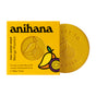 A yellow box of Anihana Feel-Good Soap, illustrated with mango and passionfruit, sits next to a round yellow sustainable soap featuring an embossed design.