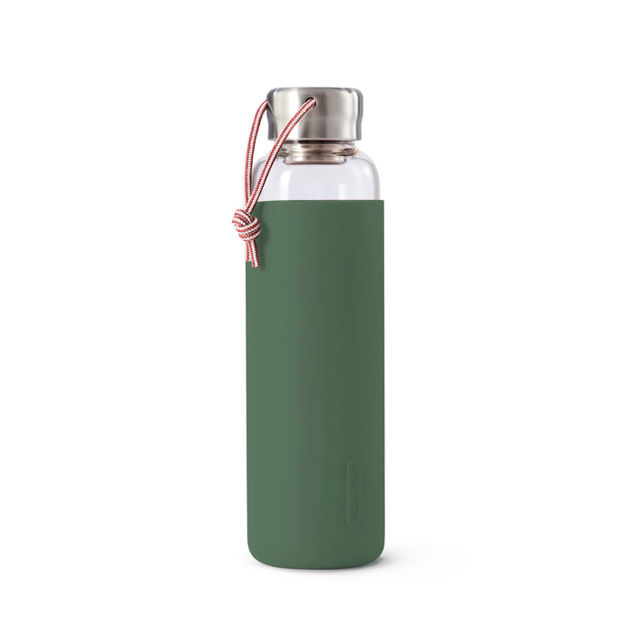 The Black + Blum Glass Water Bottle features a green silicone sleeve, stainless steel lid, and a red-and-white carrying cord attached to the cap for easy transport.