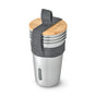The Black + Blum Steel Cup Set of 4 includes stainless steel cups topped with a bamboo wooden lid that serves as a chopping board, all secured with a gray fabric strap and featuring the Black + Blum logo.