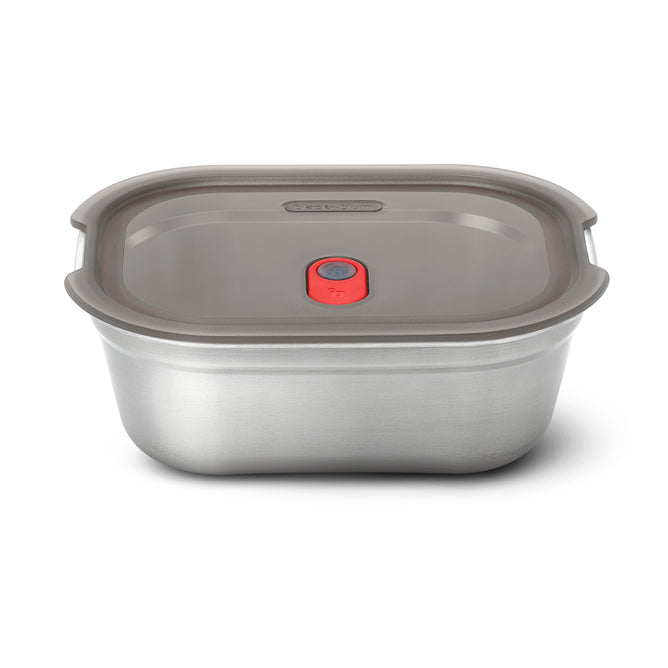The Black + Blum Steel Food Box is a rectangular, microwaveable stainless steel container with a gray plastic lid featuring a red center button that fits securely and is leakproof.