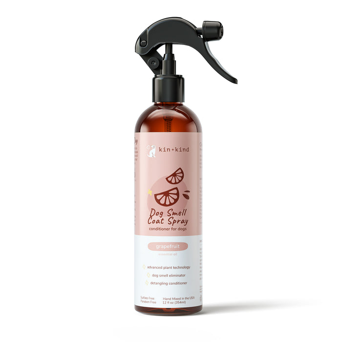 A bottle of kin+kind Dog Smell Coat Spray with a spray nozzle, featuring a pink label with grapefruit illustrations. The label notes it is a conditioner for dogs with deodorizing and detangling properties.