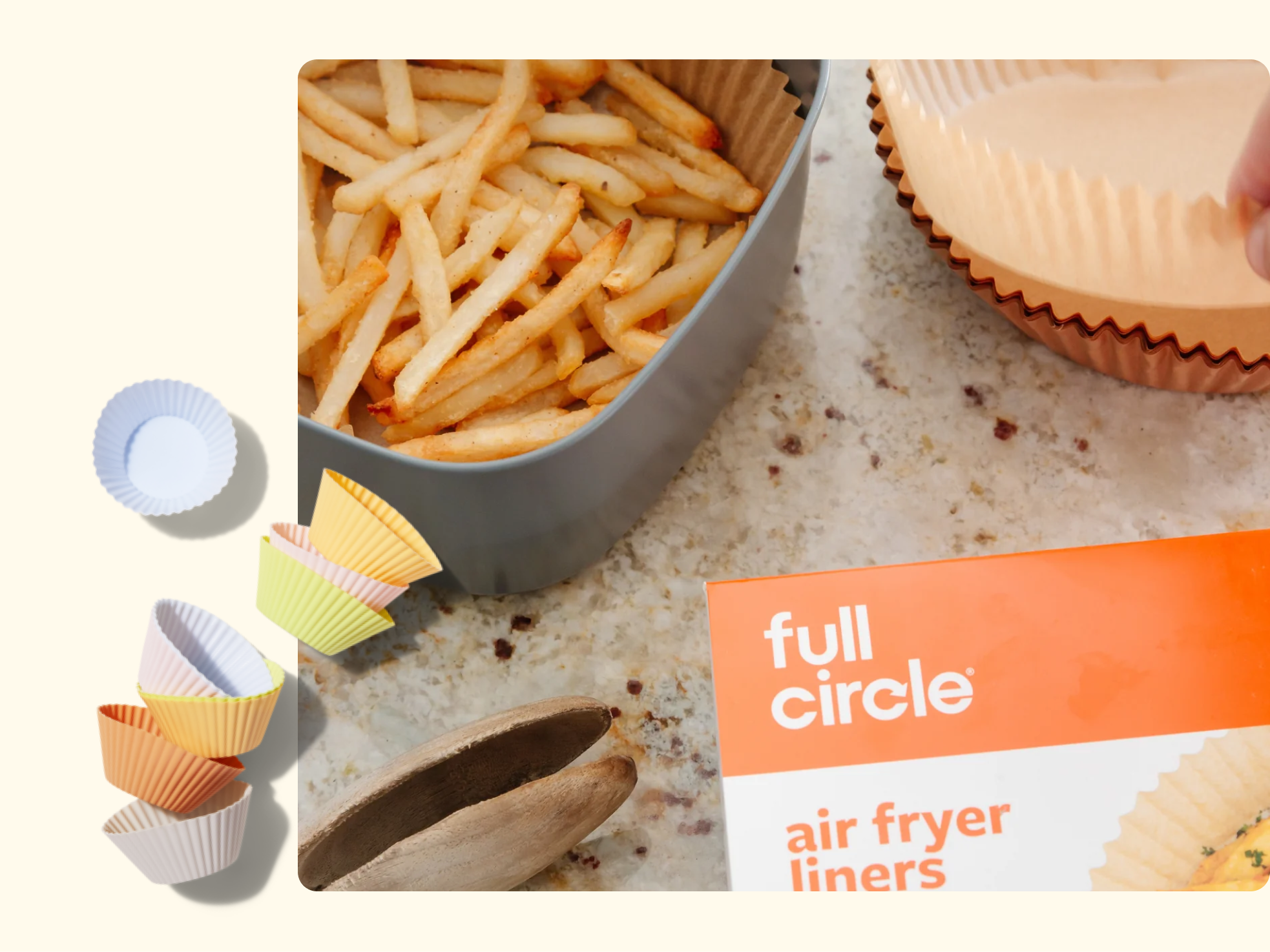 A box of Full Circle air fryer liners sits on a countertop beside a container of French fries, several colorful liners, and a wooden salad tong. A hand is placing a liner into a tray.