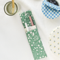 On a white tablecloth, Esembly Baby’s 4-pack Reusable Silicone Sipper Straws and their green upcycled storage pouch sit beside a glass honey jar, blueberries in a blue gingham bowl, and a plate with yellow flower designs.