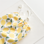 The Esembly Baby Reusable Paper Towel Set (100% Organic, Unbleached) is pictured in a lemon-patterned drawstring bag on a textured white surface, with a white button and string nearby—ideal for stylish, eco-friendly storage.