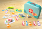 A teal carrying case, die, animal figurines, medical tool cards, and bandage tokens from the HABA My Very First Games - Let’s Be Veterinarians, 2+ Years game spread out on a wooden floor for veterinary role play.