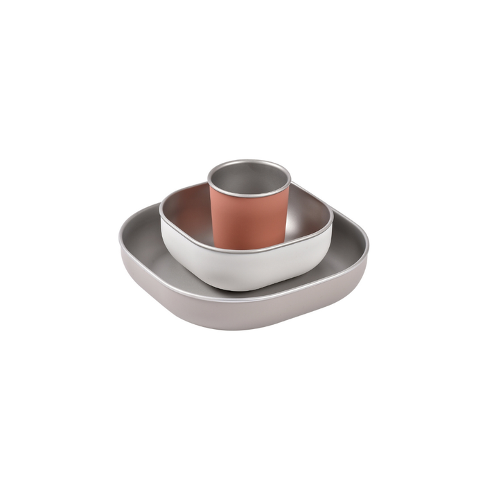 The BEABA Stainless Steel Meal Set features modern, minimalist tableware with ergonomic design: a square plate, rounded bowl, and a cup with muted pink exterior, all stacked together on a white background.