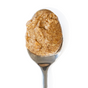 A metal spoon holds a scoop of Big Spoon Roasters Pistachio Crunch Almond Butter—made with California pistachios—against a white background.