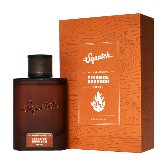 A brown bottle of Dr. Squatch Spray Cologne is shown beside its matching orange box with wood grain patterns and a fire icon; both display white product text.