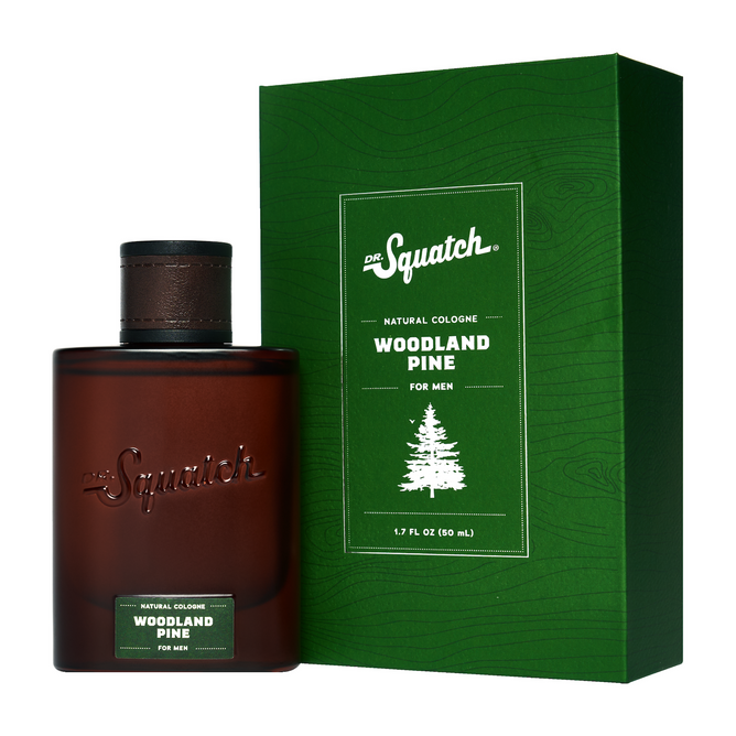 A bottle of Dr. Squatch Spray Cologne sits next to its green box with white text and a pine tree graphic. The brown bottle with a dark cap and green label highlights this men's fragrance made from sustainable ingredients.