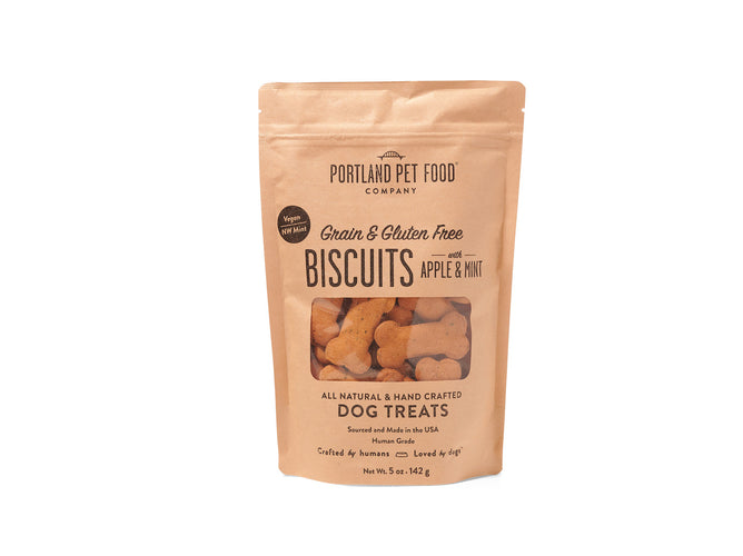 A 5 oz (142 g) brown paper bag of Portland Pet Food Companys Grain & Gluten-Free Dog Biscuits, made with human-grade ingredients like apple and mint using Bobs Red Mill Flour, features a clear window displaying bone-shaped treats crafted from Pacific Northwest elements.