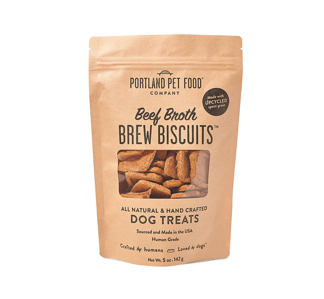 A tan pack of Upcycled Dog Brew Biscuits from Portland Pet Food Company, made with spent grains and beef broth, has a see-through window showing the natural, handcrafted treats inside that dogs adore.