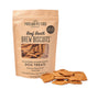 A bag of Portland Pet Food Companys Upcycled Dog Brew Biscuits is open, showcasing the tempting treats inside. Several nutritious brew biscuits made from spent grains are scattered invitingly in front of the brown paper bag.