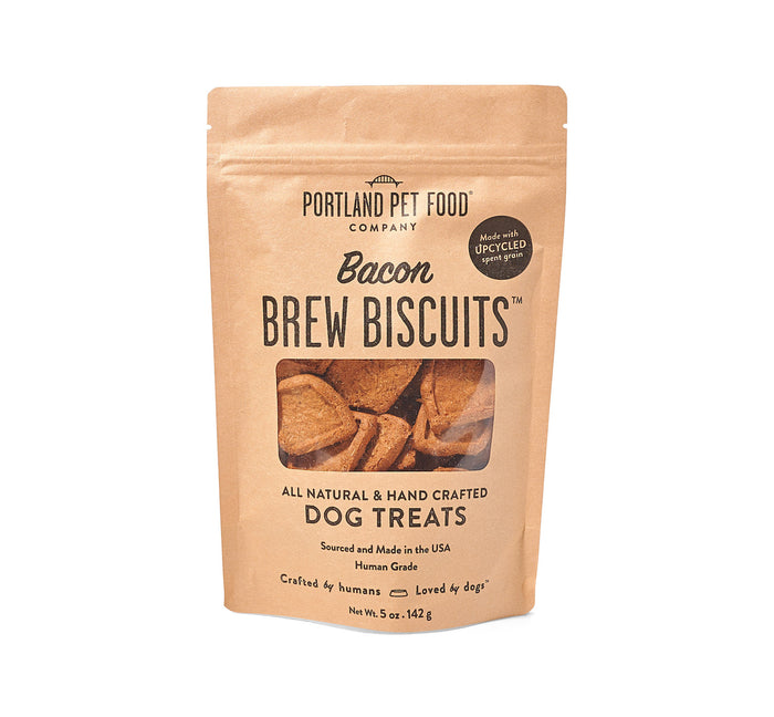 Portland Pet Food Companys Upcycled Dog Brew Biscuits comes in a brown paper bag with a small window, highlighting the human-grade, upcycled spent grains for quality and sustainable dog treats.